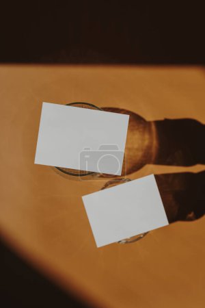 Téléchargez les photos : Cartes en papier vierges avec espace de copie maquette, lunettes, ombres de lumière du soleil sur fond orange. Modèle de marque d'entreprise minimaliste bohème esthétique. Couché plat, vue du dessus - en image libre de droit