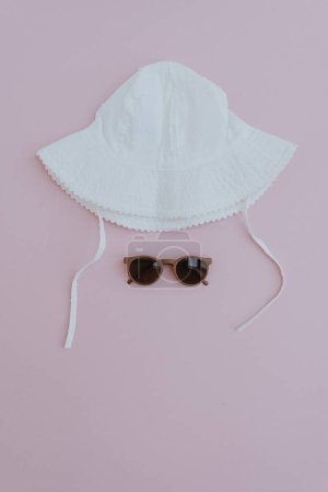 Photo for Summer baby accessories. Panama hat and sunglasses on pastel pink background. Flat lay, top view minimalist baby fashion set - Royalty Free Image