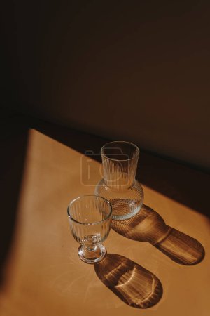 Téléchargez les photos : Champaign glass and glass vase on warm tan orange background with sun light shades silhouette. Aesthetic minimalist composition - en image libre de droit