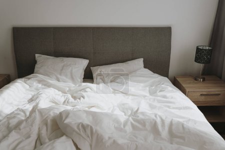 Foto de Estética casa minimalista, dormitorio de diseño interior. Cama con ropa de cama blanca arrugada, almohadas, sombras de luz solar - Imagen libre de derechos