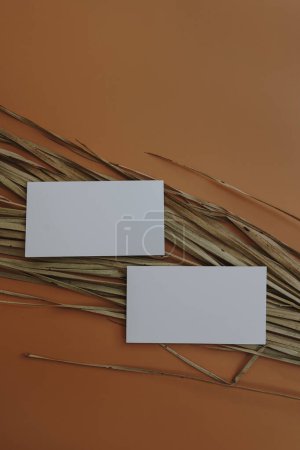 Photo for Branding or invitation card template. Blank paper invitation card sheet with empty mock up copy space. Dry palm leaf on orange background. Flat lay, top view - Royalty Free Image