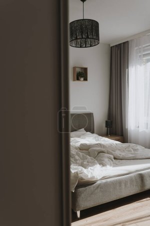 Foto de Diseño interior del dormitorio estético. Neutro escandinavo cómodo salón con cama, ropa de cama arrugada, ventana con cortinas. Sombras de luz solar - Imagen libre de derechos