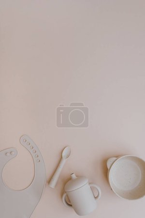 Photo for Set of silicone bowl, spoon, bib, mug for little baby kid to eat food and drink. Light pastel pink background. Flat lay, top view - Royalty Free Image