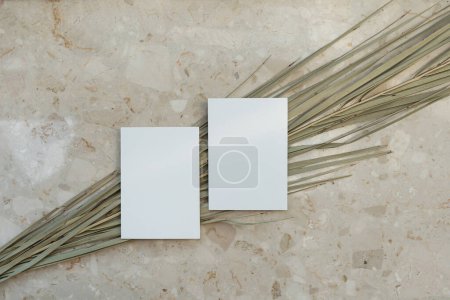 Photo for Blank paper invitation cards with copy space. Dried tropical palm leaf stem on marble stone background. Flat lay, top view aesthetic minimalist wedding invitations - Royalty Free Image