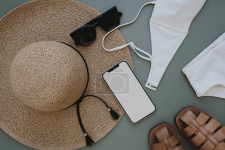 Téléchargez les photos : Flatlay of aesthetic women's fashion accessories. Mobile phone with blank copy space screen. Stylish female straw hat, swimsuit, sunglasses, sandals on pastel background. Top view, flat lay - en image libre de droit