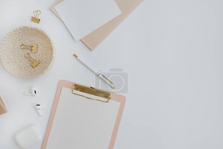 Téléchargez les photos : Flatlay of stylish female accessories and office stuff. Comfortable home office workspace. Work at home. Clipboard, clips, wireless headphones pen on table - en image libre de droit