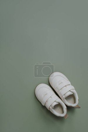 Téléchargez les photos : Chaussures mini baskets blanches. Chaussures bébé sur fond vert pastel doux. Mode vêtements scandinaves pour enfants. Couché plat, vue du dessus - en image libre de droit