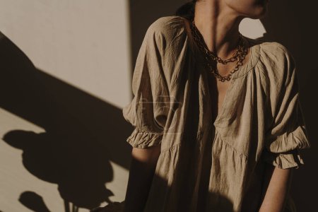 Foto de Mujer bonita joven en vestido de lino beige neutro, vestido en sombras de luz solar. Elegante estilo de vida estético bohemio de lujo composición elegante de moda. Ropa de moda con reflejos de sombra de luz solar - Imagen libre de derechos