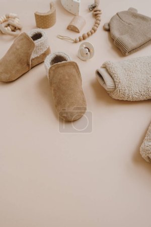 Photo for Warm winter children's suede booties, jacket, hat, pacifier, toys. Baby clothes and accessories set on neutral beige background. Fashion Scandinavian children's clothes - Royalty Free Image