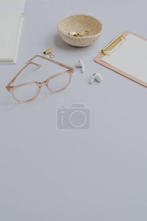 Photo for Clipboard, wireless headphones, glasses, clips in rattan plate. Minimal business copy space template for social media, magazine, blog. Home office desk table workspace - Royalty Free Image