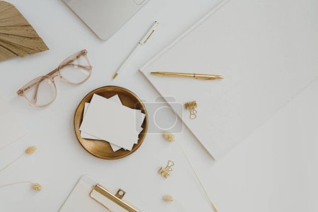 Photo for Paper card sheet with blank empty mockup copy space on gold plate. Aesthetic elegant office desk workspace with glasses and golden colour stationery. Minimalist invitation, branding card template - Royalty Free Image