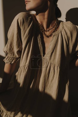 Photo for Young pretty woman in linen dress and against the wall. Silhouette in sunlight. Shadows on the wall. Minimal fashion design concept. Aesthetic - Royalty Free Image