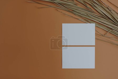 Foto de Hojas de tarjetas de papel con espacio de copia maqueta en blanco, hoja de palma seca sobre fondo naranja. Invitación mínima bohemia de lujo o plantilla de tarjeta de visita - Imagen libre de derechos
