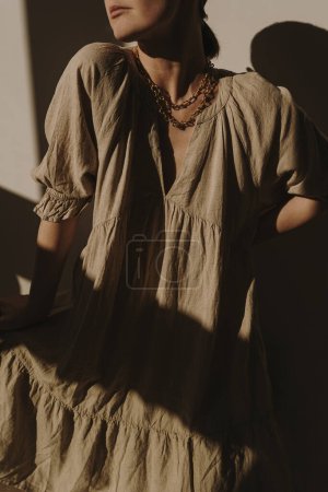 Photo for Woman in beige dress, sundress, gold necklace. Aesthetic warm sunlight shadows. Elegant bohemian fashion wearing. Online shopping, sale, store concept - Royalty Free Image