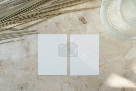 Photo for Paper card sheet with blank mockup copy space, dried palm leaf, glass vase on marble background. Aesthetic sunlight shadow silhouette. Luxury bohemian minimal invitation or business card template - Royalty Free Image