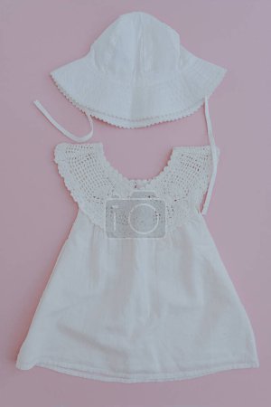 Téléchargez les photos : Ensemble de vêtements d'été mignon pour bébé fille sur fond rose. Robe blanche et chapeau panama. Pose plate, vue du dessus de la sélection de mode élégante pour petit bébé - en image libre de droit