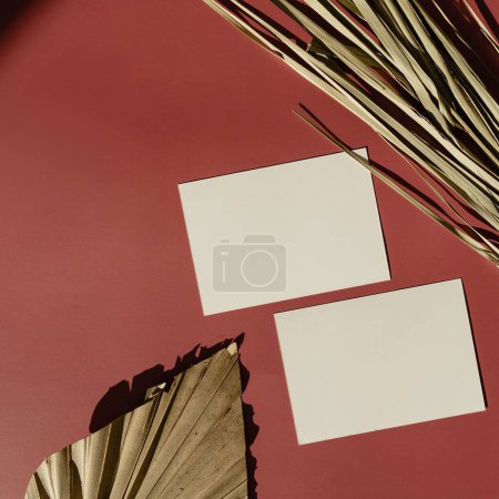 Photo for Blank paper sheet card with mockup copy space on red background with sunlight shadows silhouette. Dry tropical palm leaf. Aesthetic bohemian minimal business brand template. Flat lay, top view - Royalty Free Image