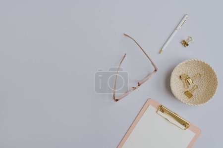 Photo for Flatlay of gold female accessories and office stuff. Comfortable home office workspace. Work at home. Clipboard, glasses, clips, pen on pastel table. Flat lay, top view - Royalty Free Image