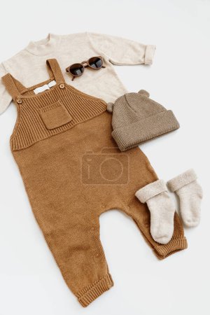 Photo for Set of knitted baby romper jumpsuit, jumper sweater, hat, sunglasses, socks on white background. Gender neutral baby clothes and accessories. Flat lay, top view - Royalty Free Image