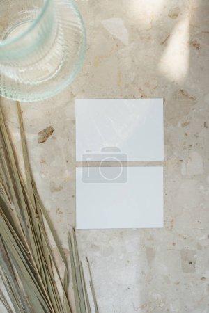 Téléchargez les photos : Carte de feuille de papier avec espace de copie maquette vierge et feuille de palme séchée sur fond de table en marbre avec silhouette ombragée en lumière douce du soleil - en image libre de droit