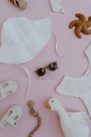 Téléchargez les photos : Stylish cute newborn baby summer clothes, accessories and toys on pastel pink background. Dress, panama hat, shoes, sunglasses. Neutral pastel pink color. Flat lay, top view - en image libre de droit