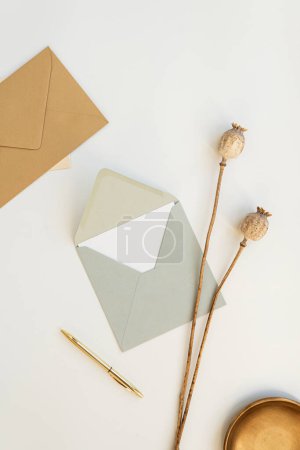 Téléchargez les photos : Cartes d'invitation Flatlay, enveloppes artisanales, tiges de pavot, stylo sur fond blanc. Couché plat, vue du dessus - en image libre de droit