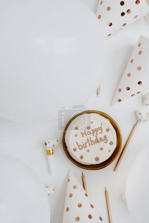 Téléchargez les photos : Pose plate avec gâteau d'anniversaire blanc et or, ballons, chapeaux de fête, bougies sur la table. Vue de dessus fête fête fête événement concept célébration - en image libre de droit