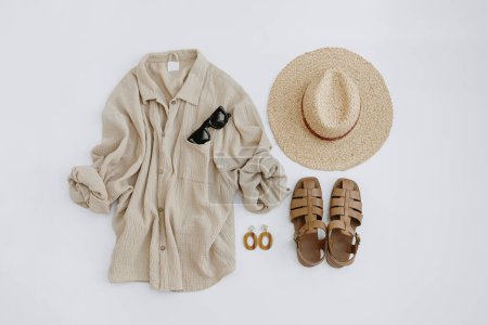 Photo for Flatlay of elegant stylish women's beach clothes and accessories. Aesthetic luxury summer fashion composition. Muslin t-shirt, straw hat, leather sandals, sunglasses, earrings. Flat lay, top view - Royalty Free Image