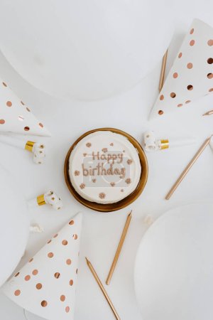 Foto de Feliz cumpleaños. Pastel de cumpleaños, globos, pasteles de fiesta, velas, decoraciones. Colores blanco y dorado. Piso tendido, vista superior - Imagen libre de derechos