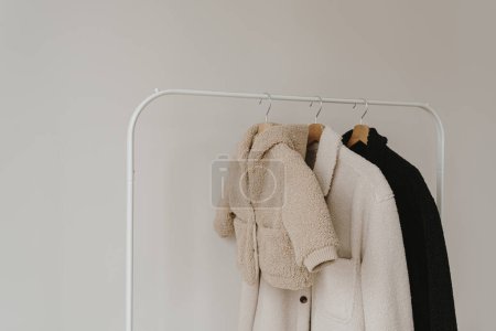 Photo for Warm autumn seasonal baby and adult clothes on hanger over white wall. Woolen neutral beige, white and black jackets. Minimalist fashion clothes wardrobe - Royalty Free Image