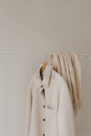 Téléchargez les photos : Veste et jupe saisonnières en laine chaude blanche d'automne sur cintre au-dessus du mur blanc. Armoire minimaliste de vêtements de mode - en image libre de droit