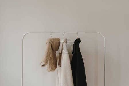 Foto de Bebé de lana esponjosa y chaquetas para adultos en percha. Fondo de armario de moda minimalista - Imagen libre de derechos