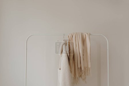 Téléchargez les photos : Veste et jupe saisonnières en laine chaude blanche d'automne sur cintre au-dessus du mur blanc. Armoire minimaliste de vêtements de mode - en image libre de droit