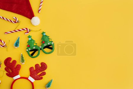 Téléchargez les photos : Nouvel An drôle, accessoires de Noël pour la fête des vacances d'hiver fête sur fond jaune. Lunettes de Noël, cannes à bonbons, cornes de cerf, chapeau de Père Noël, arbres jouets - en image libre de droit