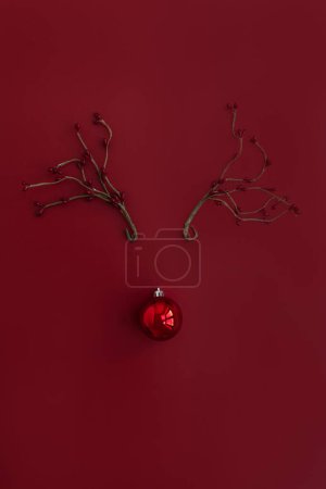Foto de Vista superior de bolas de chucherías y rama de bayas dispuestas en venado de Navidad con cuernos sobre fondo rojo carmesí. Piso tendido, vista superior - Imagen libre de derechos