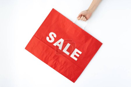 Photo for Hand holding red craft shopping bag with sign SALE. Minimal Black Friday shopping, sale, promotion advertising concept - Royalty Free Image