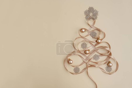 Foto de Vista superior de bolas de bolas, estrellas y cintas dispuestas en árbol de Navidad con juguetes sobre fondo beige pastel - Imagen libre de derechos