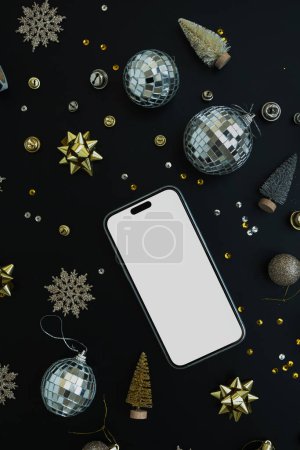 Photo for Flatlay of blank clipping path screen mobile phone. Disco balls, golden stars, toy Christmas trees, sparkling confetti on black background. Luxury aesthetic Christmas concept - Royalty Free Image