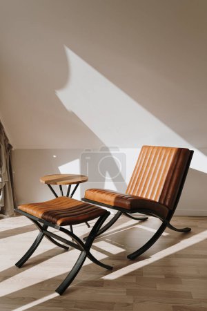 Téléchargez les photos : Intérieur moderne décoré avec fauteuil de salon en cuir. Ombres solaires chaudes esthétiques sur le mur. Concept minimaliste de design d'intérieur de maison - en image libre de droit