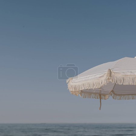 Téléchargez les photos : Minimal vacances d'été concept de vacances. Parapluie de plage devant le ciel bleu et la mer. Refroidissant, se prélasser sur la plage - en image libre de droit