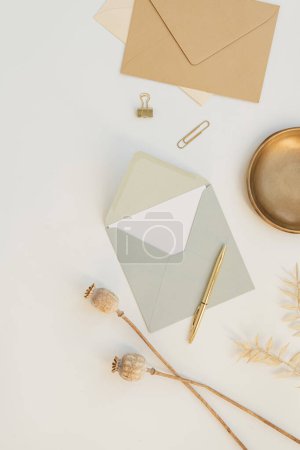 Photo for Holiday event invitation. Blank paper greeting card, craft envelope, dried poppy stems, stationery on white background. Flat lay, top view - Royalty Free Image