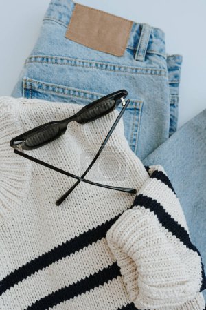 Photo for Flatlay of stylish casual women's clothes and accessories. Aesthetic minimal fashion composition. Striped sweater, blue jeans, sunglasses. Flat lay, top view - Royalty Free Image
