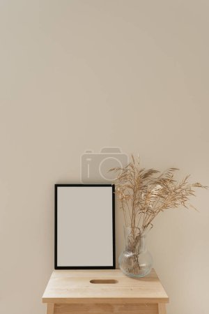 Photo for Photo frame with blank mockup copy space. Dried grass stems bouquet in glass vase on neutral beige background. Aesthetic minimal home interior design decoration - Royalty Free Image