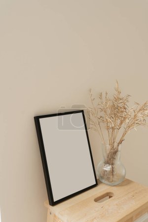 Photo for Photo frame with blank mockup copy space. Dried grass stems bouquet in glass vase on neutral beige background. Aesthetic minimal home interior design decoration - Royalty Free Image