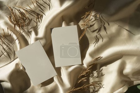 Photo for Blank paper sheet cards with mockup copy space, dried grass, soft sunlight shadows on glossy gold silk cloth. Aesthetic flat lay, top view minimal business brand template - Royalty Free Image