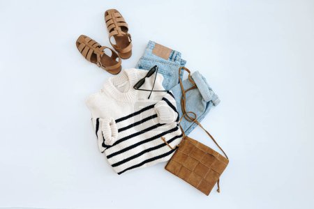 Photo for Flatlay of stylish casual women's clothes and accessories. Aesthetic fashion composition. Striped sweater, leather sandals, suede bag, jeans, sunglasses. Flat lay, top view - Royalty Free Image