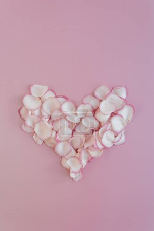 Foto de Símbolo del corazón hecho de pétalos de rosa rosa sobre fondo rosa pastel. Puesta plana, vista superior mínima composición floral - Imagen libre de derechos