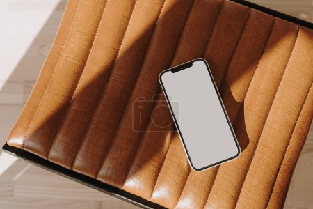 Téléchargez les photos : Téléphone portable avec écran d'espace de copie sur banc en cuir avec ombres de soleil esthétiques - en image libre de droit