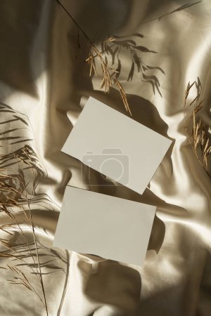 Photo for Aesthetic luxury bohemian branding or invitation cards template. Blank paper card sheet with empty mock up copy space, dried grass stems on crumpled glossy gold silk background with sunlight shadows - Royalty Free Image