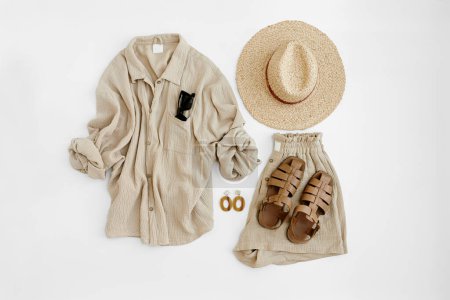 Photo for Aesthetic summer fashion composition with neutral beige female clothes and accessories. Muslin tee blouse, shorts, straw hat, leather sandals, sunglasses, earrings. Flat lay, top view. - Royalty Free Image
